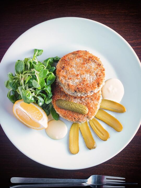 Portrait overhead image of Canned Mackerel fish cakes with pickles on a white plate against a dark backdrop