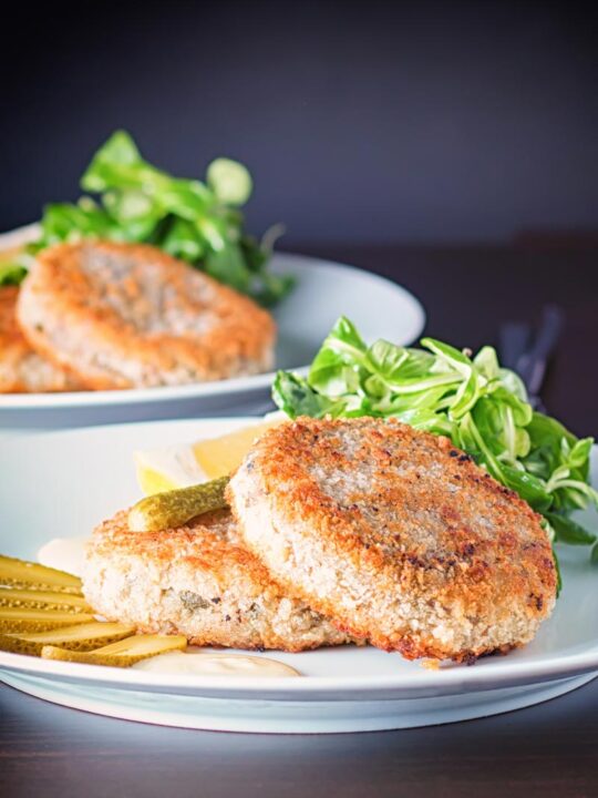 Portrait image of Canned Mackerel fish cakes with pickles on a white plate against a dark backdrop