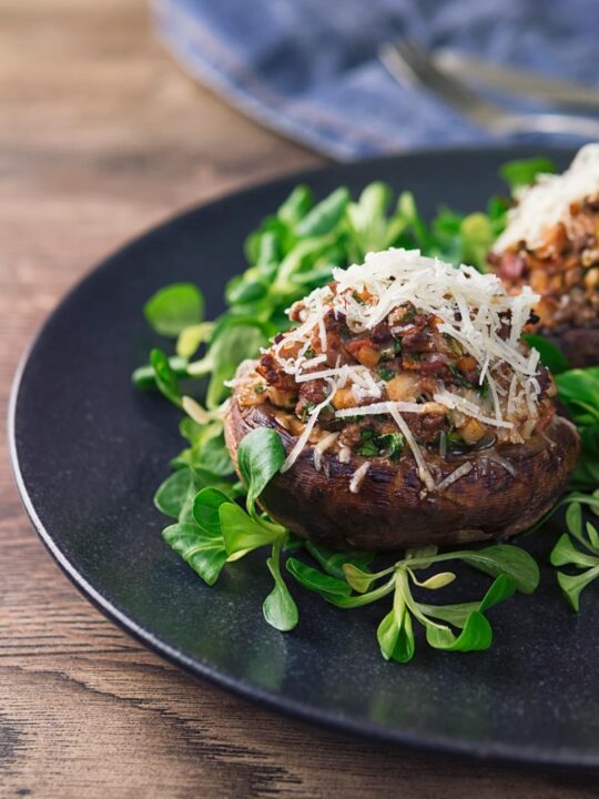 Tall image of a minced beef stuffed mushroom topped with Parmesan cheese on a wooden table