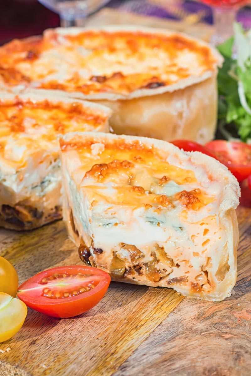 Close up portrait image of two mini cheese and onion quiche with one mini quiche cut open on a wooden chopping board in a picnic setting
