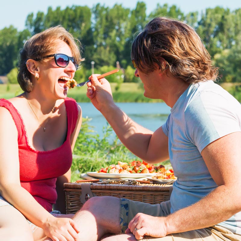 Man feeding woman a fork full of salad in a picnic setting