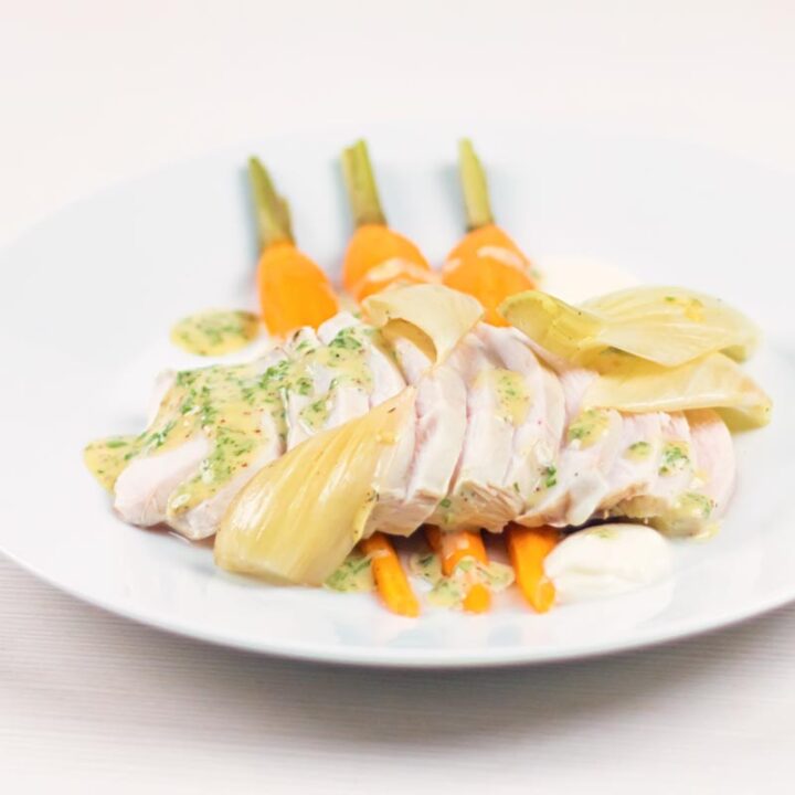 Square image of a sliced poached chicken breast on a white plate with carrots, fennel and kohlrabi puree and a mustard sauce