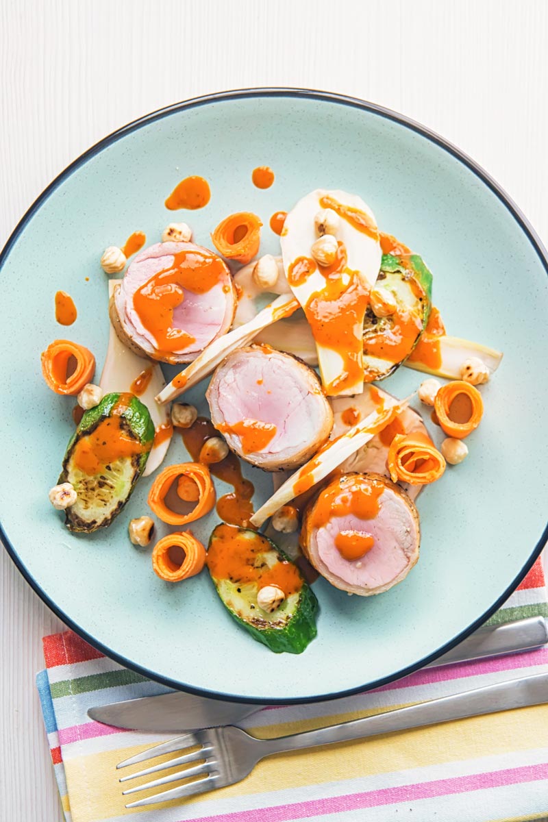 Overhead portrait image of roast pork tenderloin wrapped in bacon served with pickled carrots and pickled fennel with a harissa based dressing