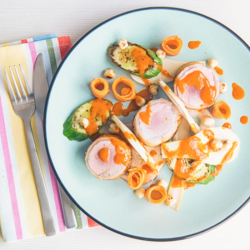 Overhead square image of roast pork tenderloin wrapped in bacon served with pickled carrots and pickled fennel with a harissa based dressing