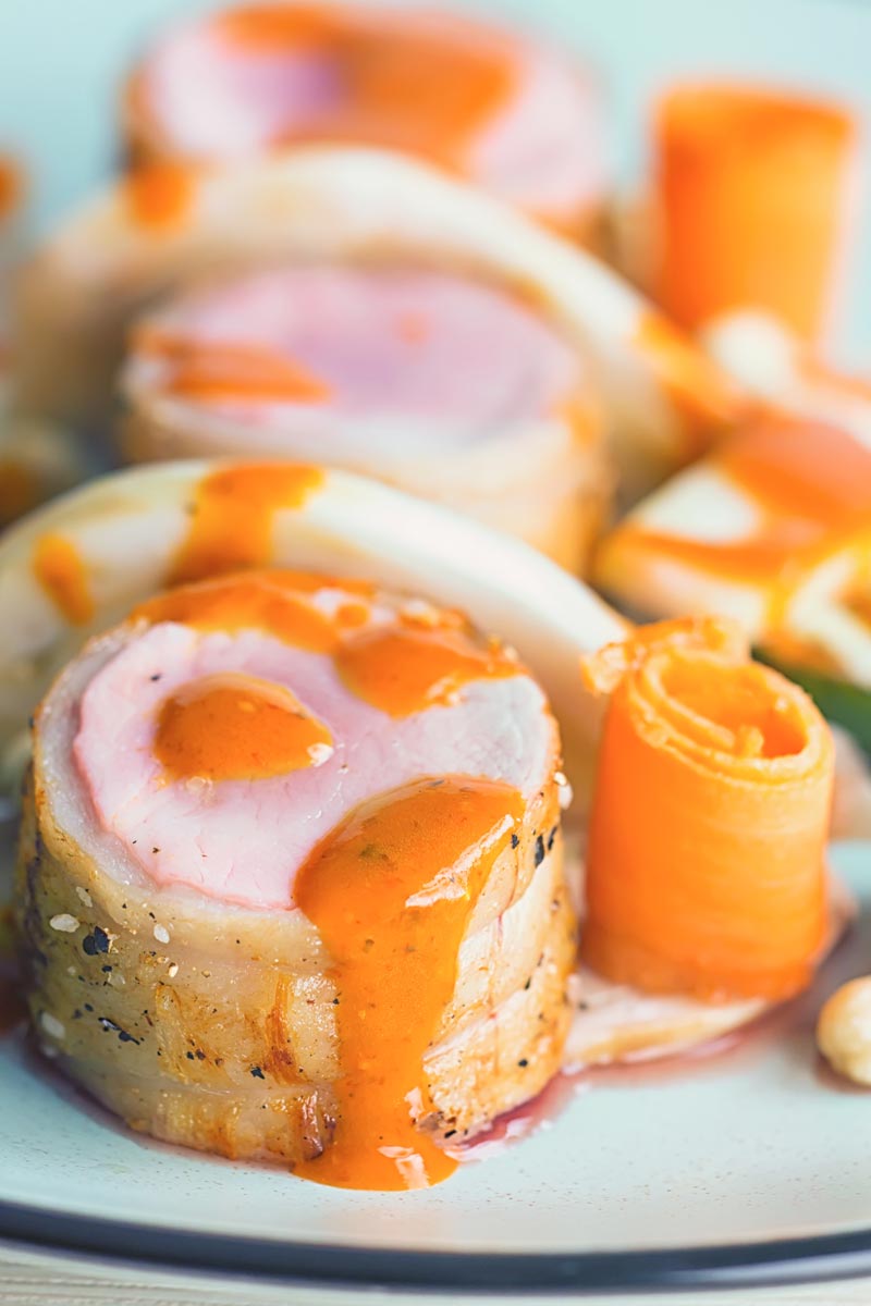 Close up portrait image image of roast pork tenderloin wrapped in bacon served with pickled carrots and a harissa based dressing