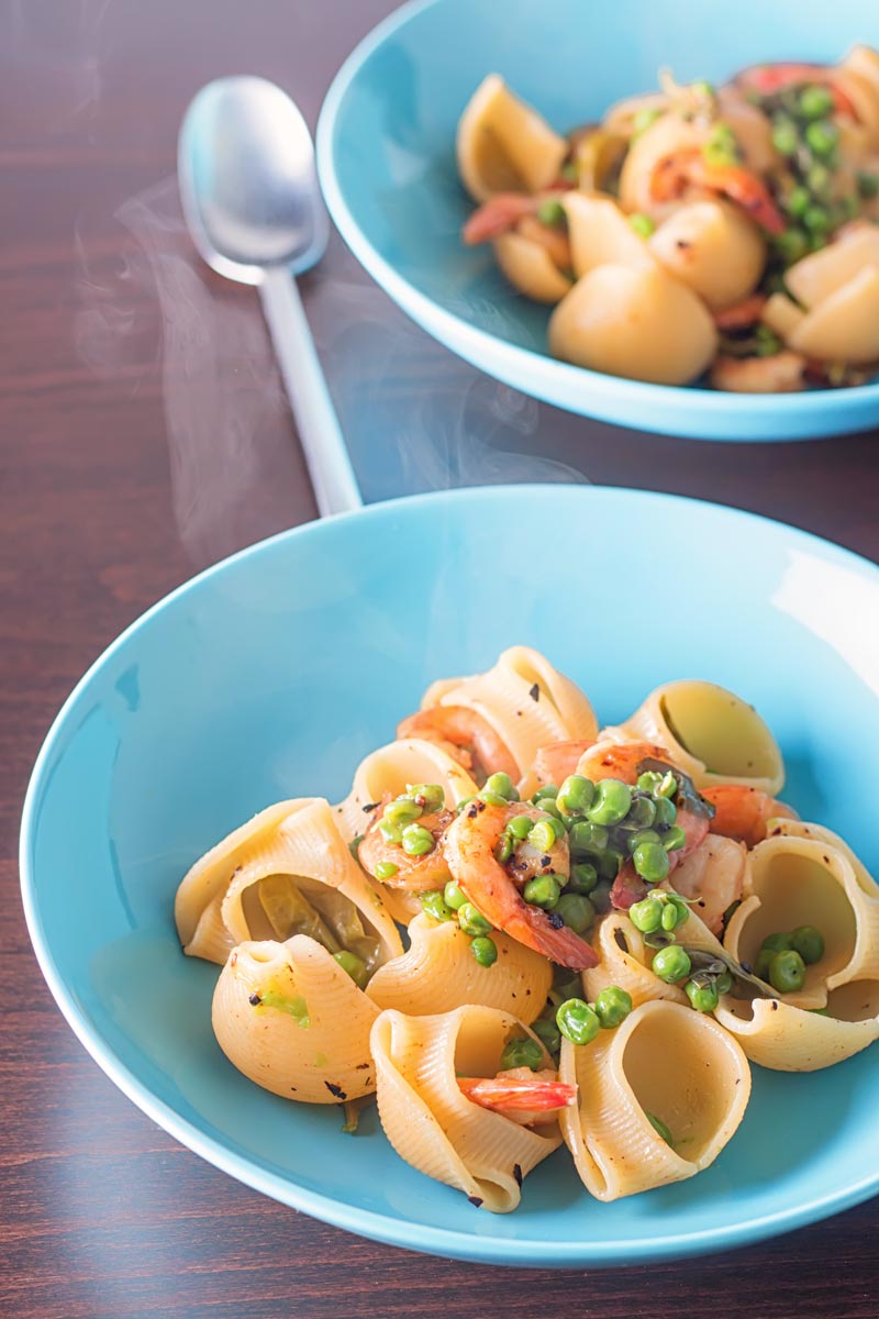 Portrait image of two steaming bowls of pea and prawn pasta served in a blue bowl
