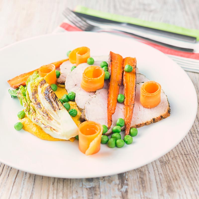 Square image of roasted pork loin slices with peas, seared lettuce, pickled carrot curls, carrot puree and roasted carrots