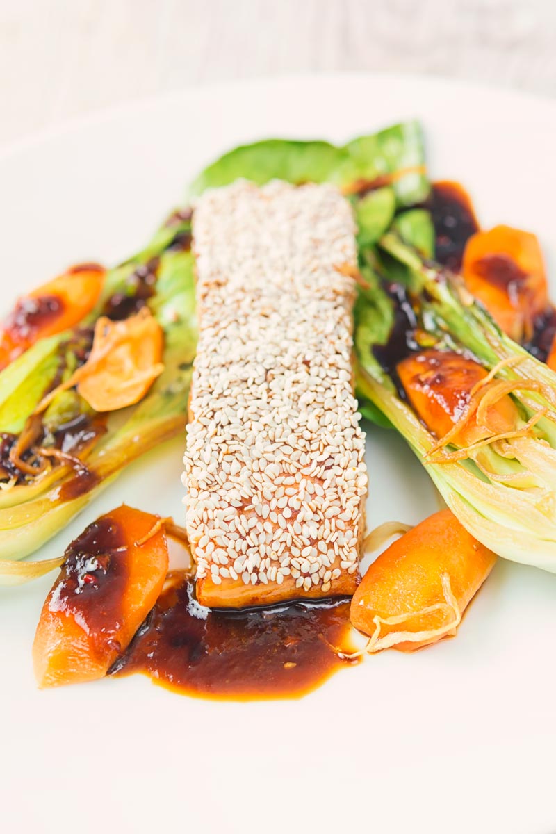 Close up portrait image of a sesame salmon fillet served with ginger bok choi and carrots on a white plate