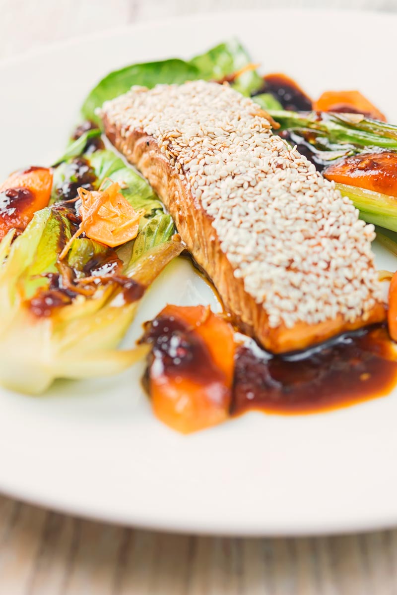 Portrait image of a sesame salmon fillet served with ginger bok choi and carrots on a white plate