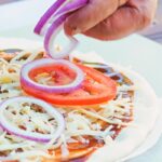Tall image of pizza being prepared with cheese tomato and red onion