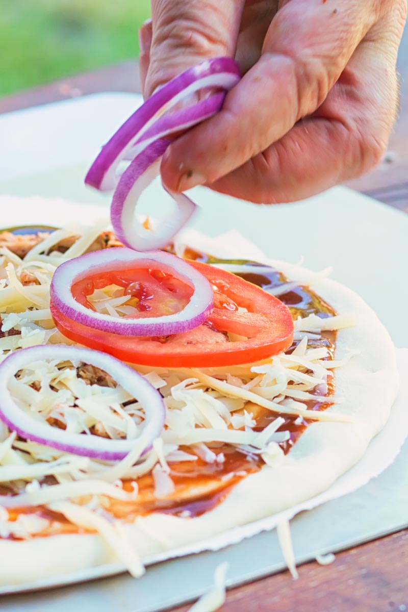 Tall image of pizza being prepared with cheese tomato and red onion