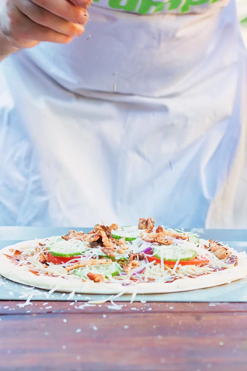 Tall image of a raw pizza being seasoned before being cooked