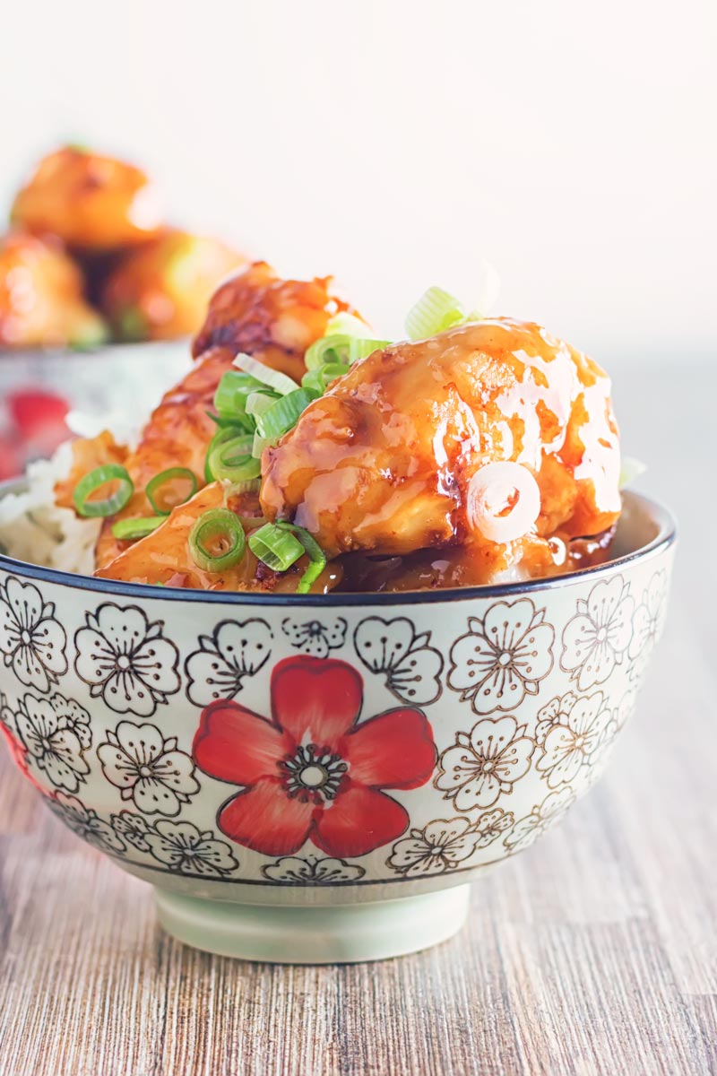 Portrait image of Chicken with Honey and Soy with a shiny glaze served in an Asian style bowl decorated with a red flower set against a white backdrop