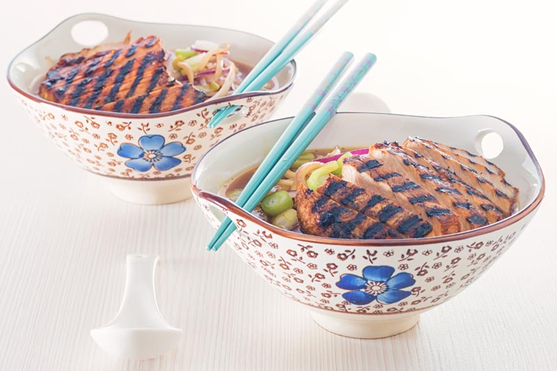 Landscape image of a spicy pork ramen noodle soup served in an Asian style bowl decorated with a blue flower