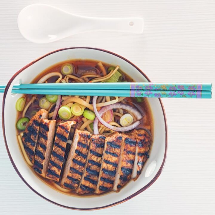 Overhead square image of a spicy pork ramen noodle soup served in a bowl with turquoise chopsticks