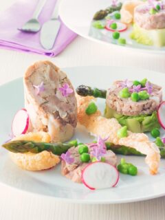 Portrait image of a spring ham hock salad, featuring pressed ham hock, asparagus, peas, lettuce, radish, and puffed pork crackling.