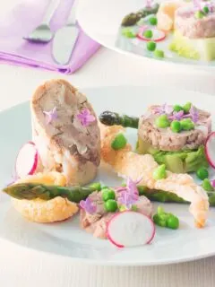 Portrait image of a spring ham hock salad, featuring pressed ham hock, asparagus, peas, lettuce, radish, and puffed pork crackling.