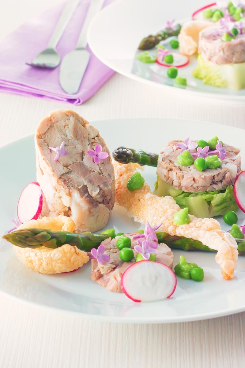 Portrait image of a spring ham hock salad, featuring pressed ham hock, asparagus, peas, lettuce, radish, and puffed pork crackling.