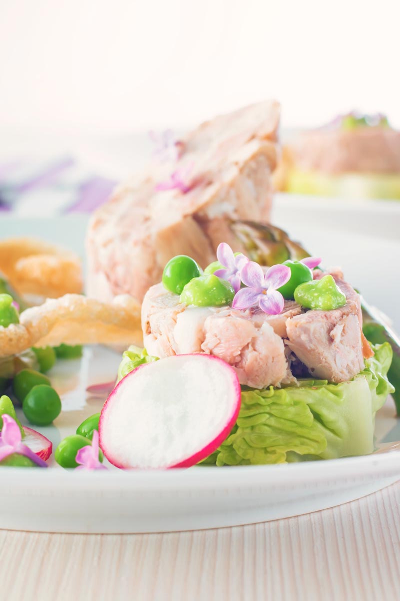 Portrait close up image of a spring ham hock salad, featuring pressed ham hock, asparagus, peas, lettuce, radish, and puffed pork crackling.