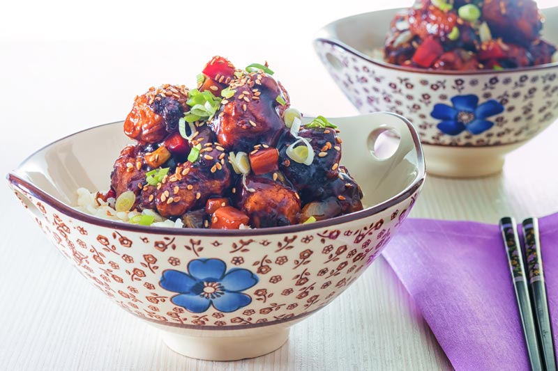 Landscape image of sweet and sour pork balls in an Asian style bowl decorated with a blue flower against a light backdrop