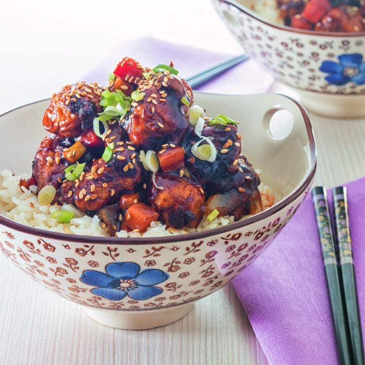 Square image of sweet and sour pork balls in an Asian style bowl decorated with a blue flower against a light backdrop