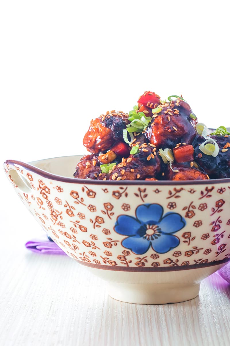 Portrait image of sweet and sour pork balls in an Asian style bowl decorated with a blue flower against a light backdrop
