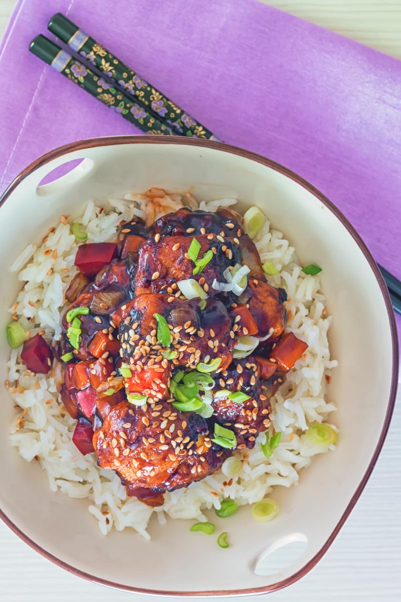 Overhead portrait image of sweet and sour pork balls in an Asian style bowl decorated with a blue flower against a light backdrop