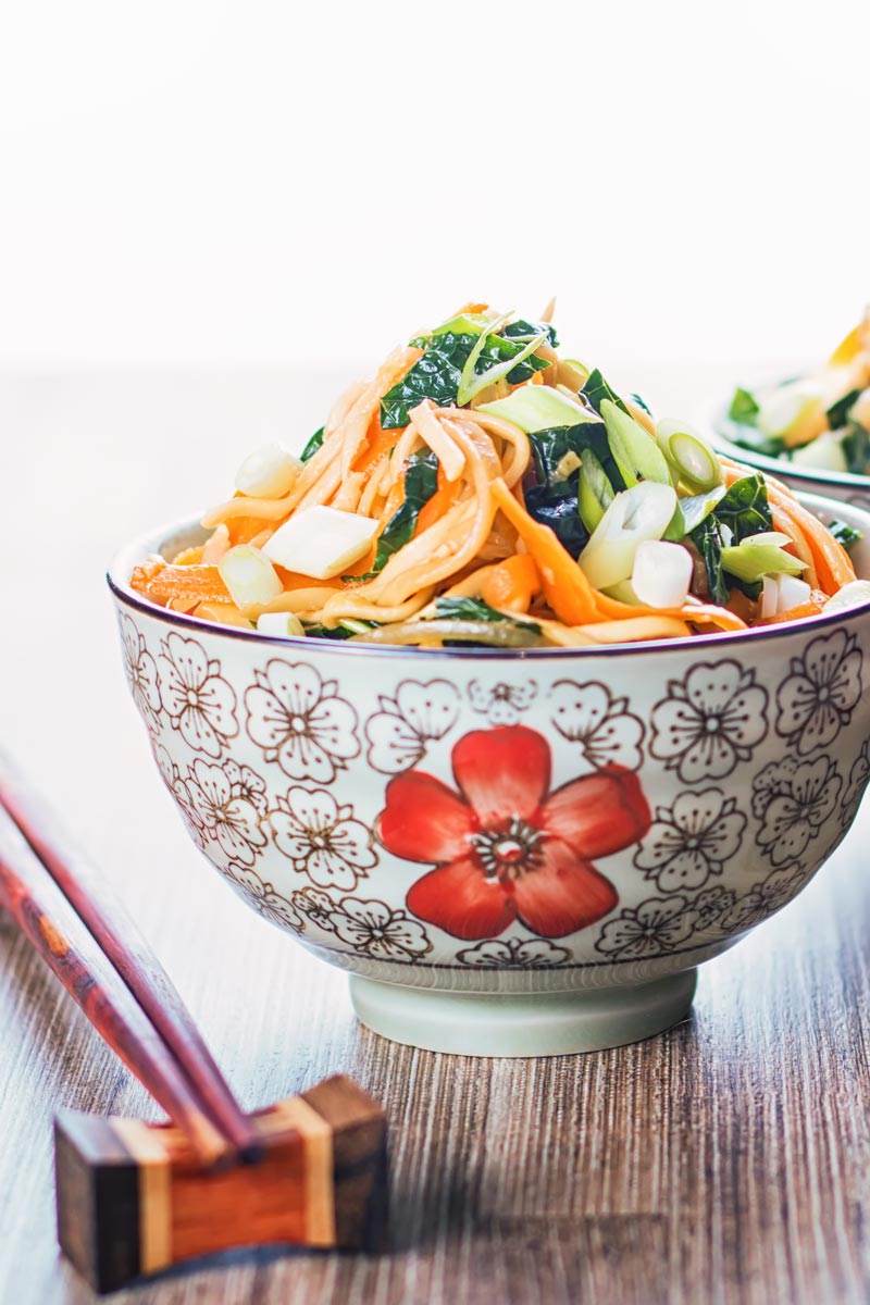 Portrait image of a bowl with Asian patterns and chopsticks containing sweet and sour Stir Fried Noodles