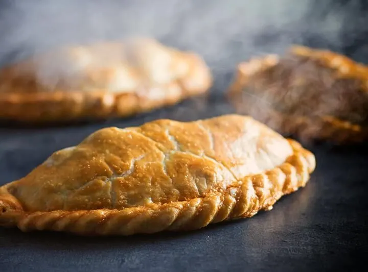 Landscape image of a traditional Cornish Pasty against a steamy dark back drop