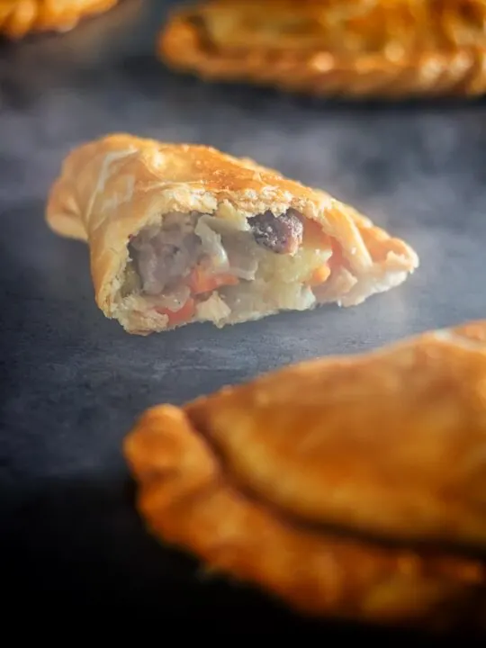 Tall image of a traditional Cornish Pasty broken open showing the filling against a steamy dark back drop
