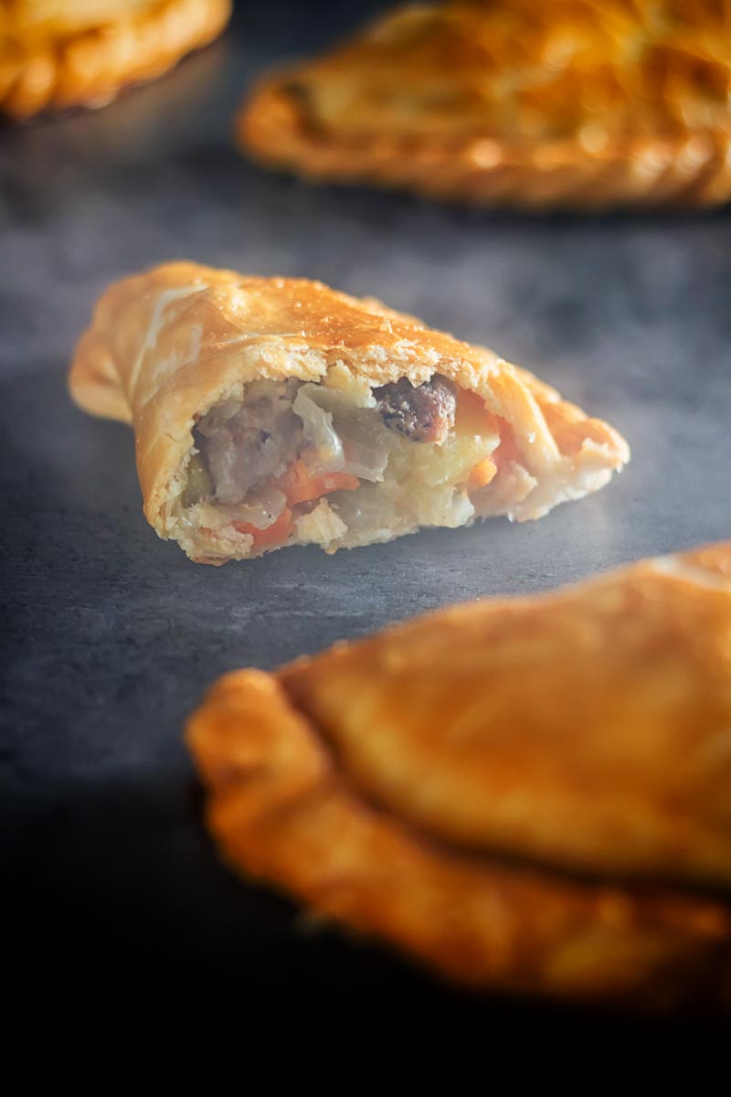 Tall image of a traditional Cornish Pasty broken open showing the filling against a steamy dark back drop