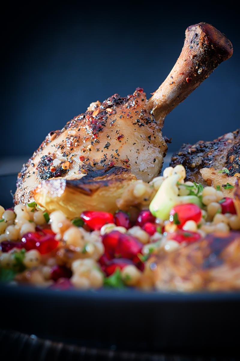Close up portrait image of zaatar chicken legs served with giant couscous, pomegranate seeds