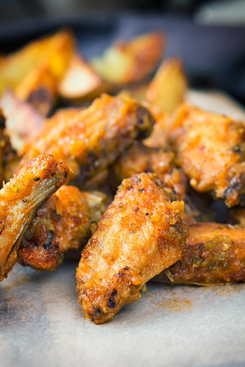 Portrait close up image of air fryer chicken wings served with potato wedges served on a wooden chopping board
