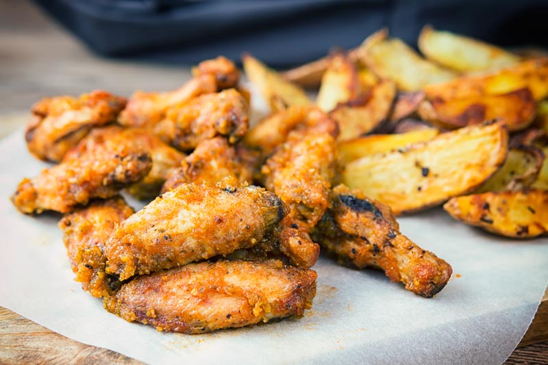 Landscape image of air fryer chicken wings served with potato wedges served on a wooden chopping board