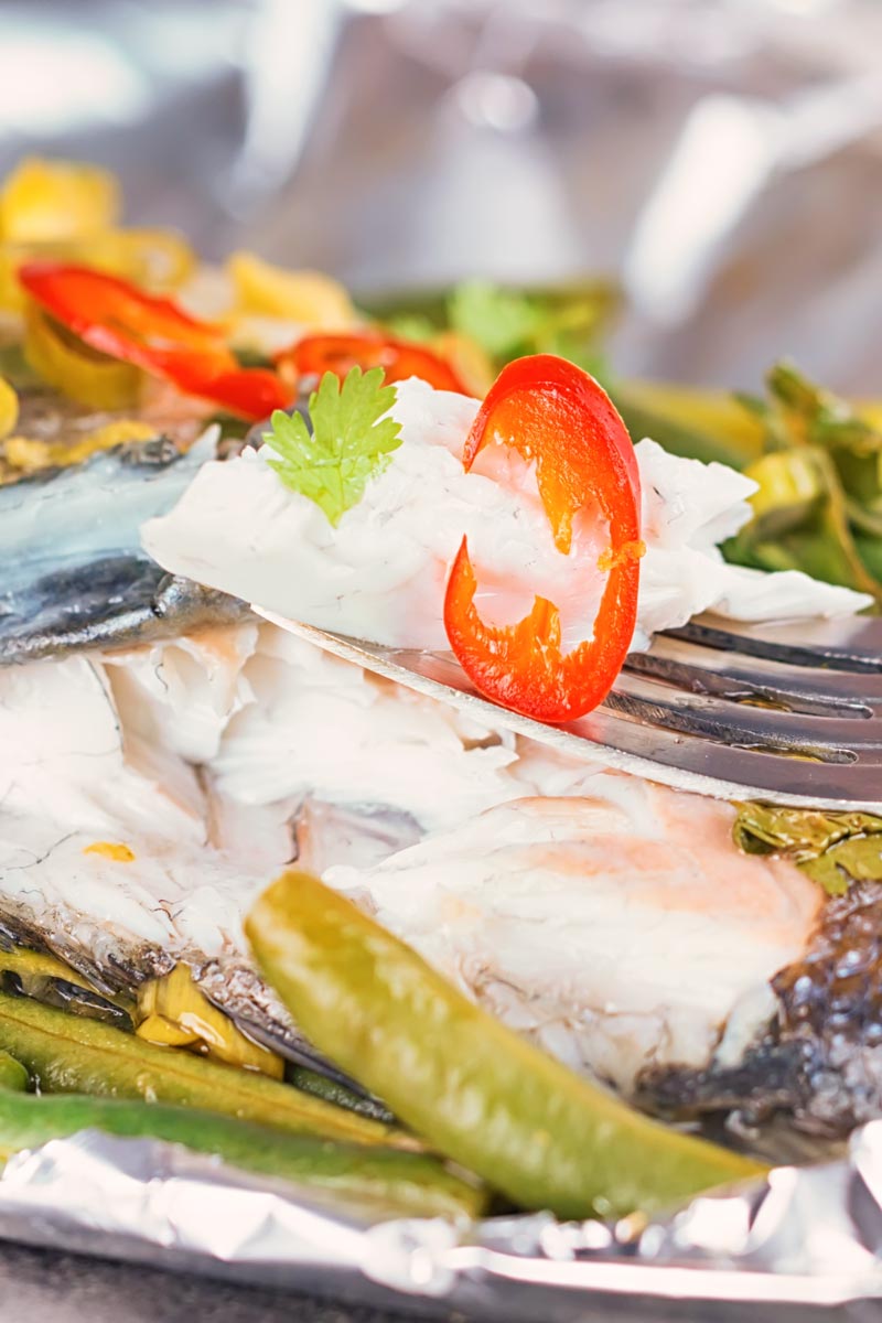 Portrait image of sea bass cooked in a foil packet en papillote showing the texture of the steamed fish