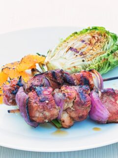 Portrait image of BBQ duck kebabs served on a white plate with grilled lettuce and seared orange segments