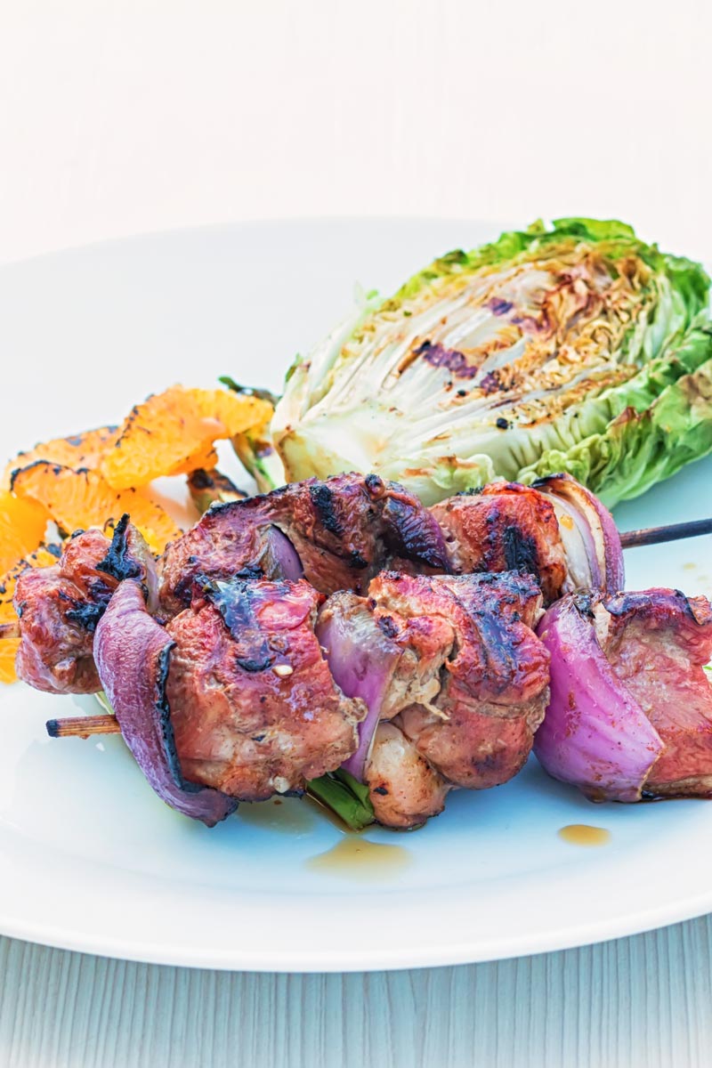 Portrait image of BBQ duck kebabs served on a white plate with grilled lettuce and seared orange segments