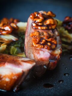 Close up portrait image of pan fried glazed duck breast with walnuts and cabbage in a balsamic sauce on a black plate