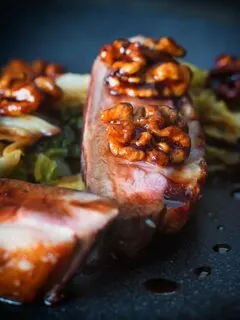 Close up portrait image of pan fried glazed duck breast with walnuts and cabbage in a balsamic sauce on a black plate