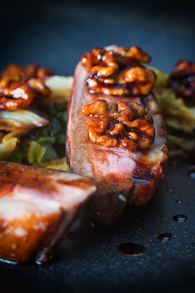 Close up portrait image of pan fried glazed duck breast with walnuts and cabbage in a balsamic sauce on a black plate