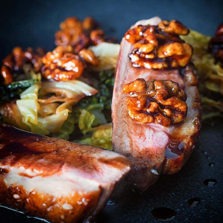 Close up square image of pan fried glazed duck breast with walnuts and cabbage in a balsamic sauce on a black plate