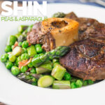 Portrait image of slowly braised beef shin on the bone served on a bed of peas, asparagus and bacon served in a white bowl with text