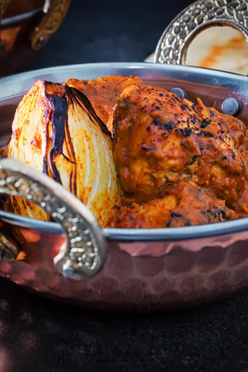 Portrait close up image of a chicken tikka masala curry served in a copper coated curry bowl