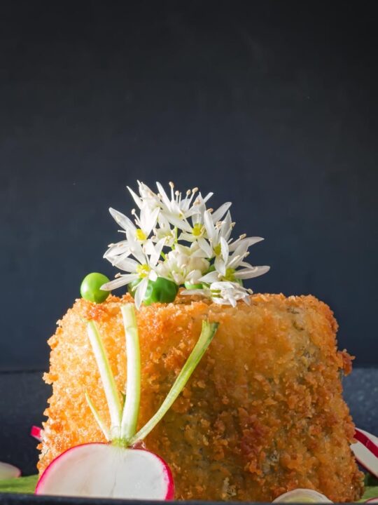 Portrait image of golden deep fried goats cheese with garlic flowers and sliced radish