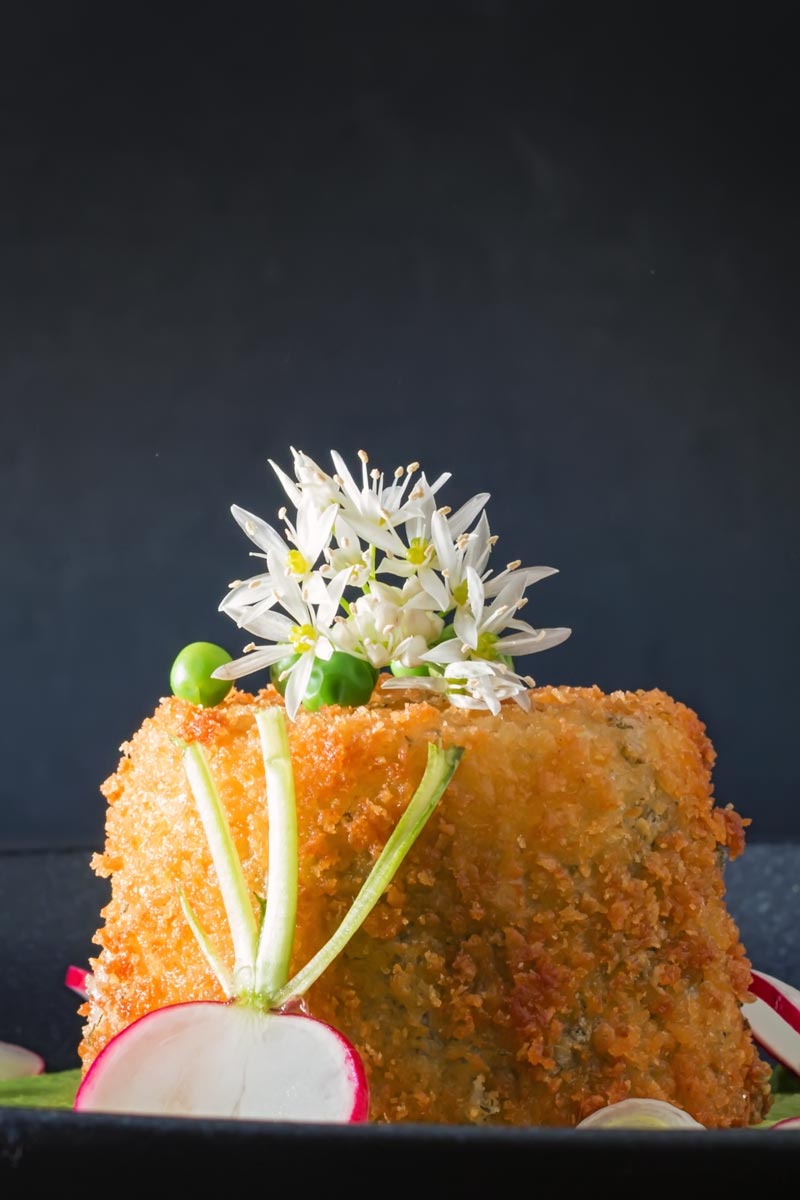 Portrait image of golden deep fried goats cheese with garlic flowers and sliced radish