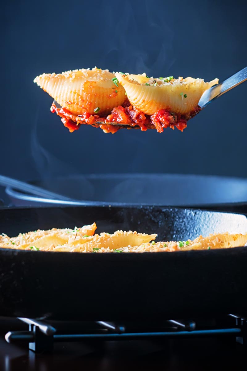 Portrait image of Goats Cheese Stuffed Pasta Shells served in a cast iron pan with two steaming pasta shells on a serving spoon