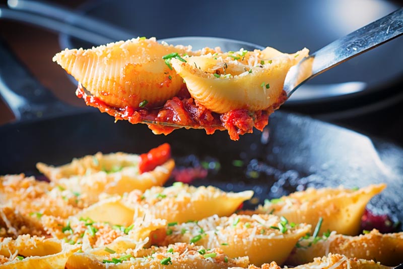 Landscape image of Goats Cheese Stuffed Pasta Shells served in a cast iron pan with two pasta shells on a serving spoon