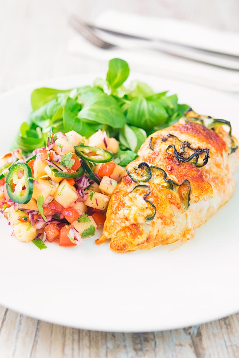 Portrait image of a roasted jalapeño and cheddar cheese stuffed chicken breast served on a white plate with pineapple salsa and a green salad