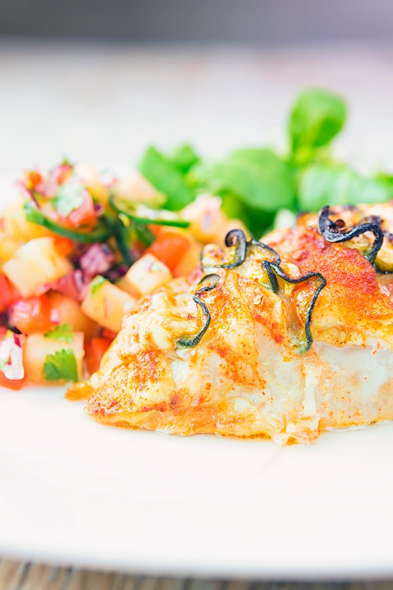 Portrait close up image of a roasted jalapeño and cheddar cheese stuffed chicken breast served on a white plate with pineapple salsa and a green salad
