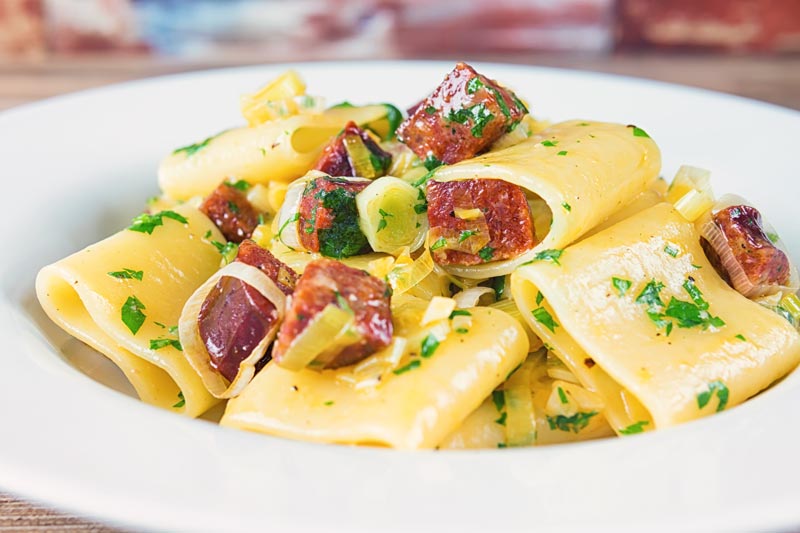 Landscape image of a leek and salami pasta with paccheri pasta served in a white bowl
